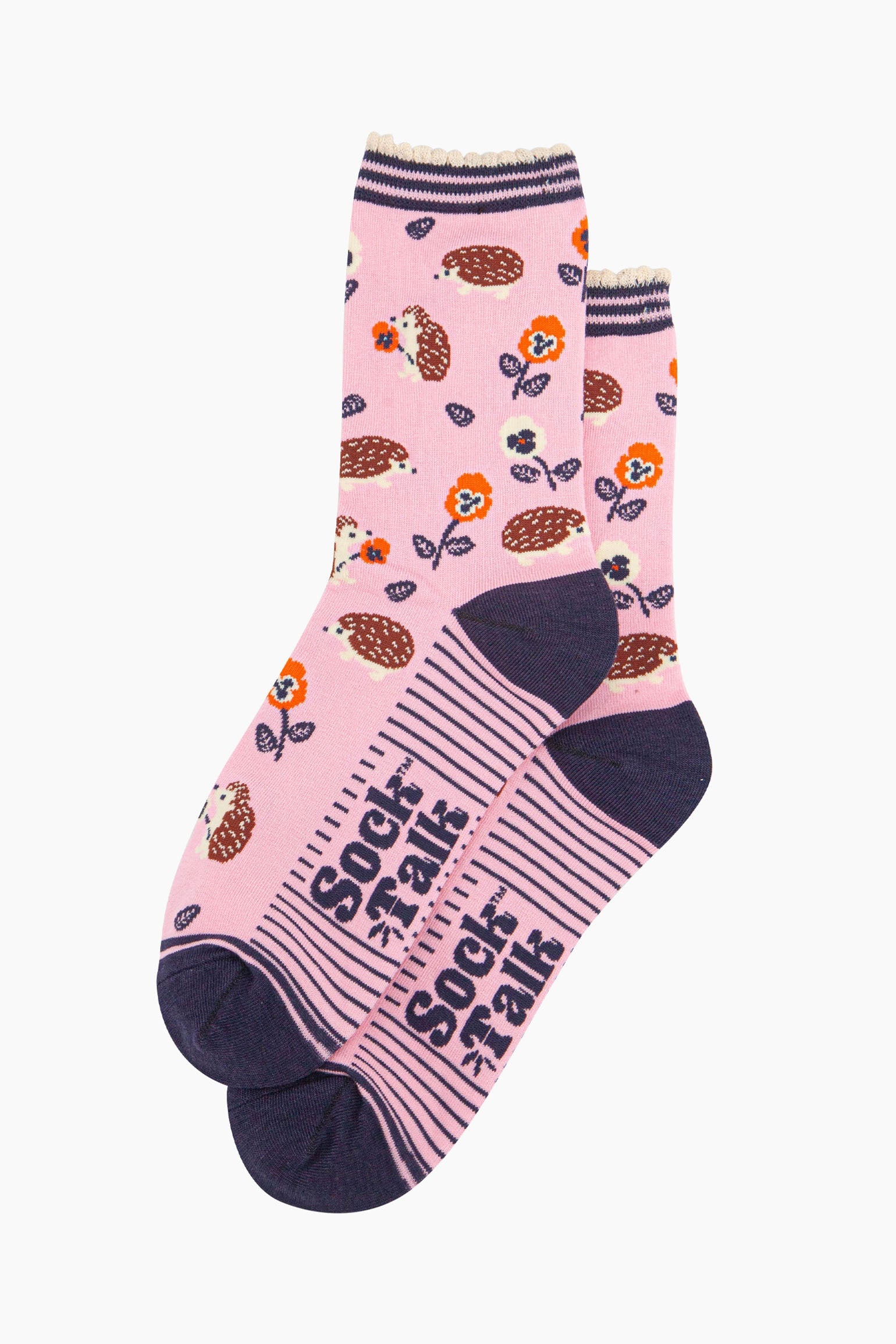 the pair of light pink hedgehog socks laying flat one overlapping the other. showing clearly the pink background of the socks which is contrasted by the all over pattern of hedgehogs, flowers and leaves.  the sock talk logo is navy blue and visible on the base of the sole.