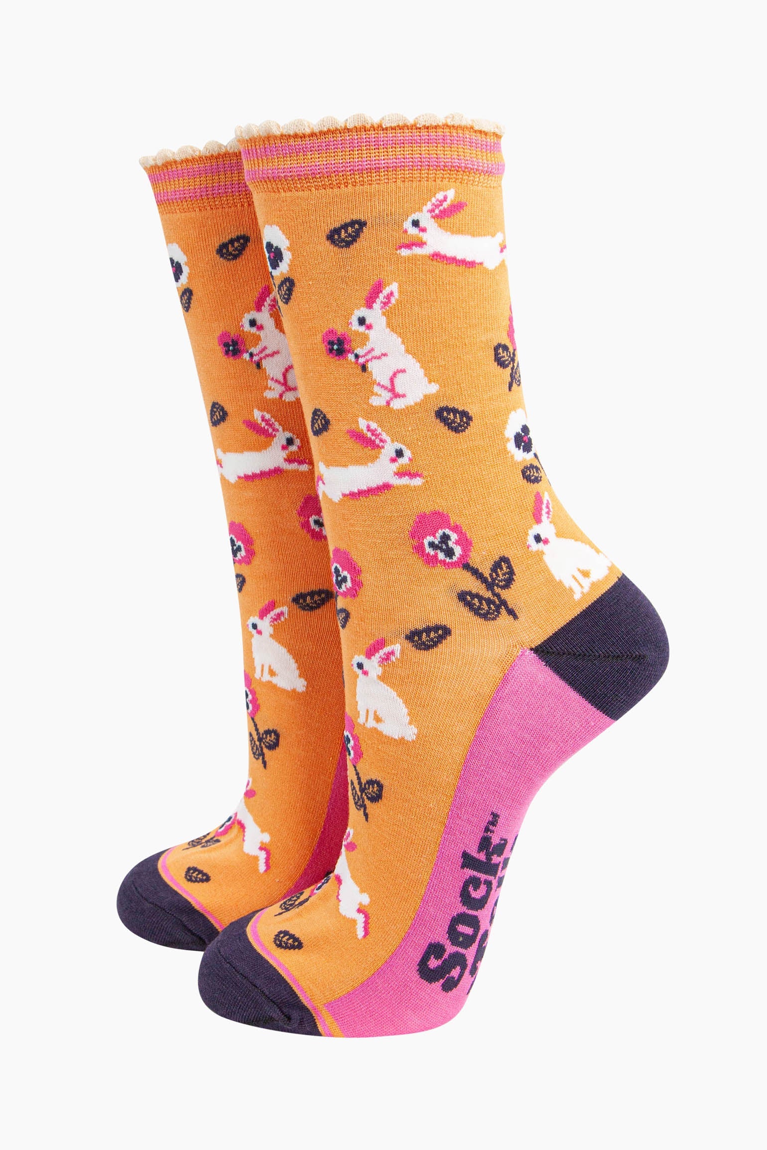 womens bamboo socks orange rabbit and flower. orange bamboo socks with a pattern of white rabbits with pink and white pansy flowers. the toe and heel are contrasting navy blue. the sole is pink with a navy blue sock talk logo visible.