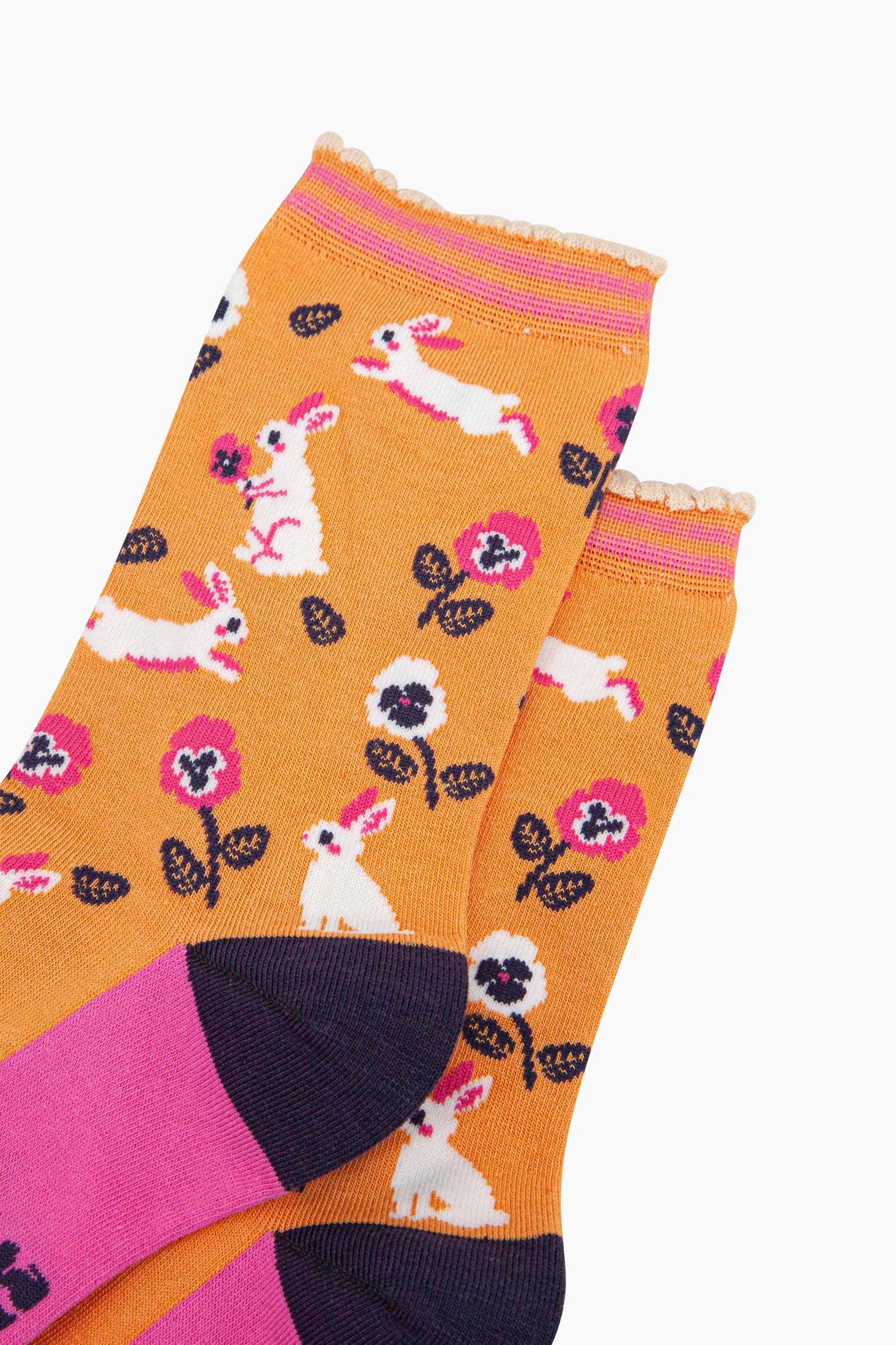 close up of the pattern, the white rabbits are running, sitting and jumping, some are holding flowers. the floral pattern features pink and white pansy like flowers. the cuff is scalloped and has a pastel orange and pink striped pattern.