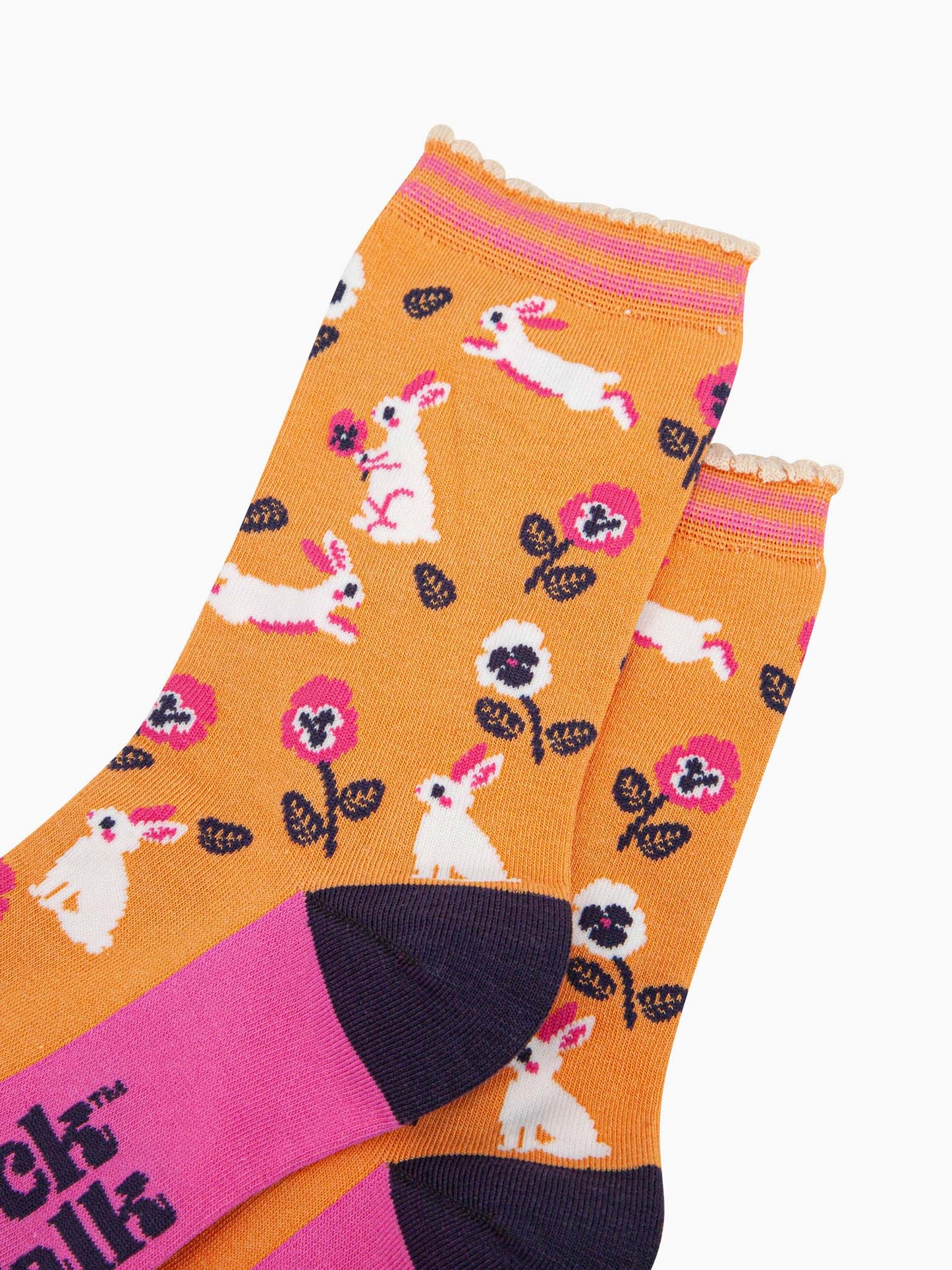 close up of the pattern, the white rabbits are running, sitting and jumping, some are holding flowers. the floral pattern features pink and white pansy like flowers. the cuff is scalloped and has a pastel orange and pink striped pattern.