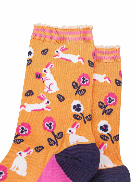 close up of the pattern, the white rabbits are running, sitting and jumping, some are holding flowers. the floral pattern features pink and white pansy like flowers. the cuff is scalloped and has a pastel orange and pink striped pattern.