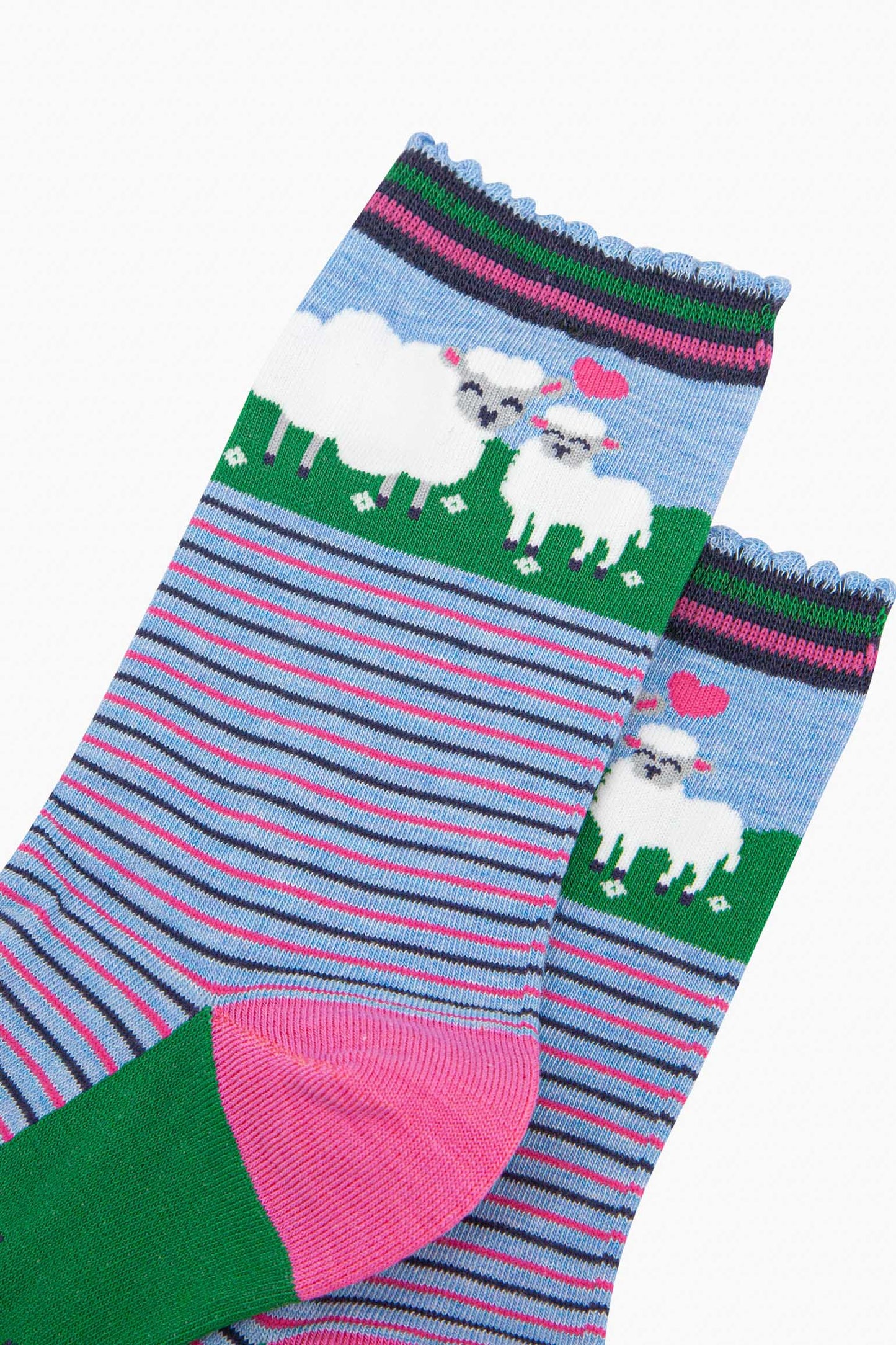 close up of the pattern, the ankle part of the socks features a white sheep and a baby lamb. between the animals is a pink love heart. the cuff of the socks is scalloped and has a pink and green stiped pattern.