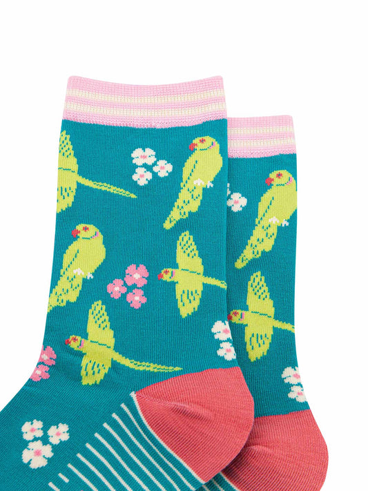 close up of the pattern. the ring necked parakeets are show flying and perching. they are lime green with red eyes and beaks. the ring on the neck is green and pink striped. interspersed among the birds are groups of three flowers in pink and white.