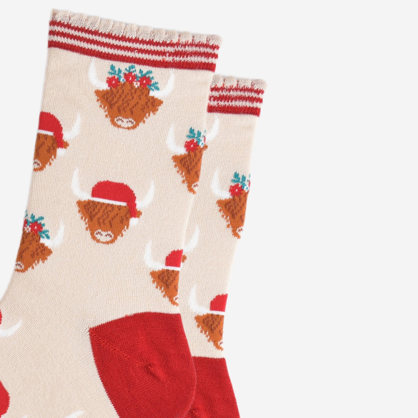 close up of the highland cow pattern on the socks, there are two designs, one with the cow wearing a red santa hat, the other the cow is wearing a festive green and red floral wreath as a crown