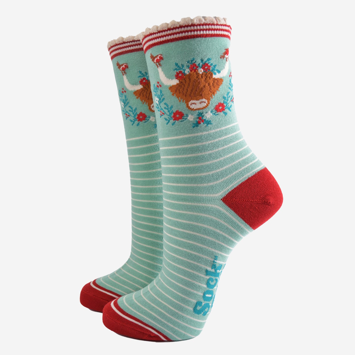 mint green bamboo socks with a large highland cow on the ankle, the highland cow is surrounded by red robin birds, and holly, the socks have a scalloped edge and a white pinstripe