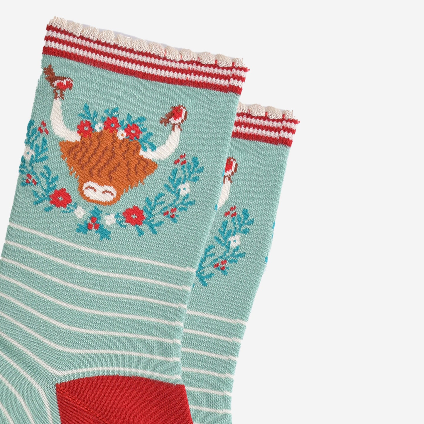 close up of the highland cow design on the ankle of the socks, there are robins perched on the tips of the horns, the wreath is green, red and yellow floral design