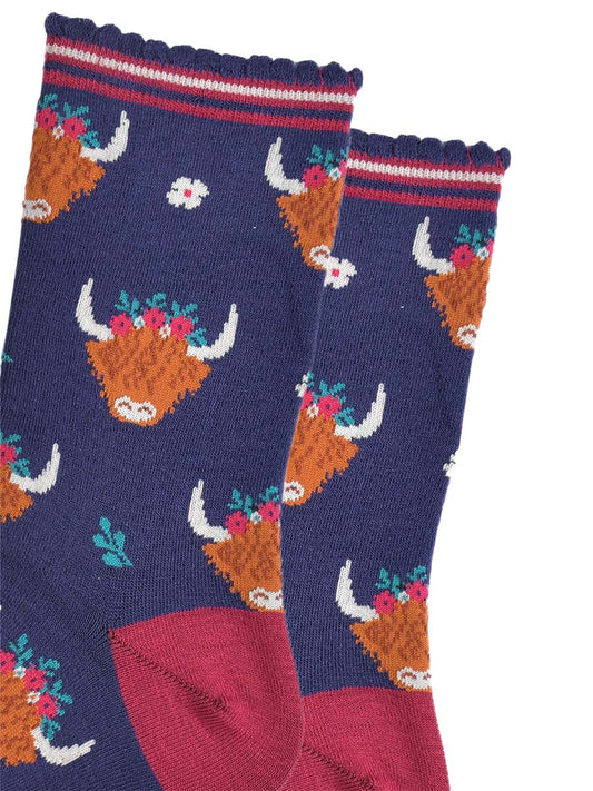 close up of the highland cow pattern on the socks, the cows are wearing green, red and white floral crowns, there are also small white flowers and green leaves on the socks