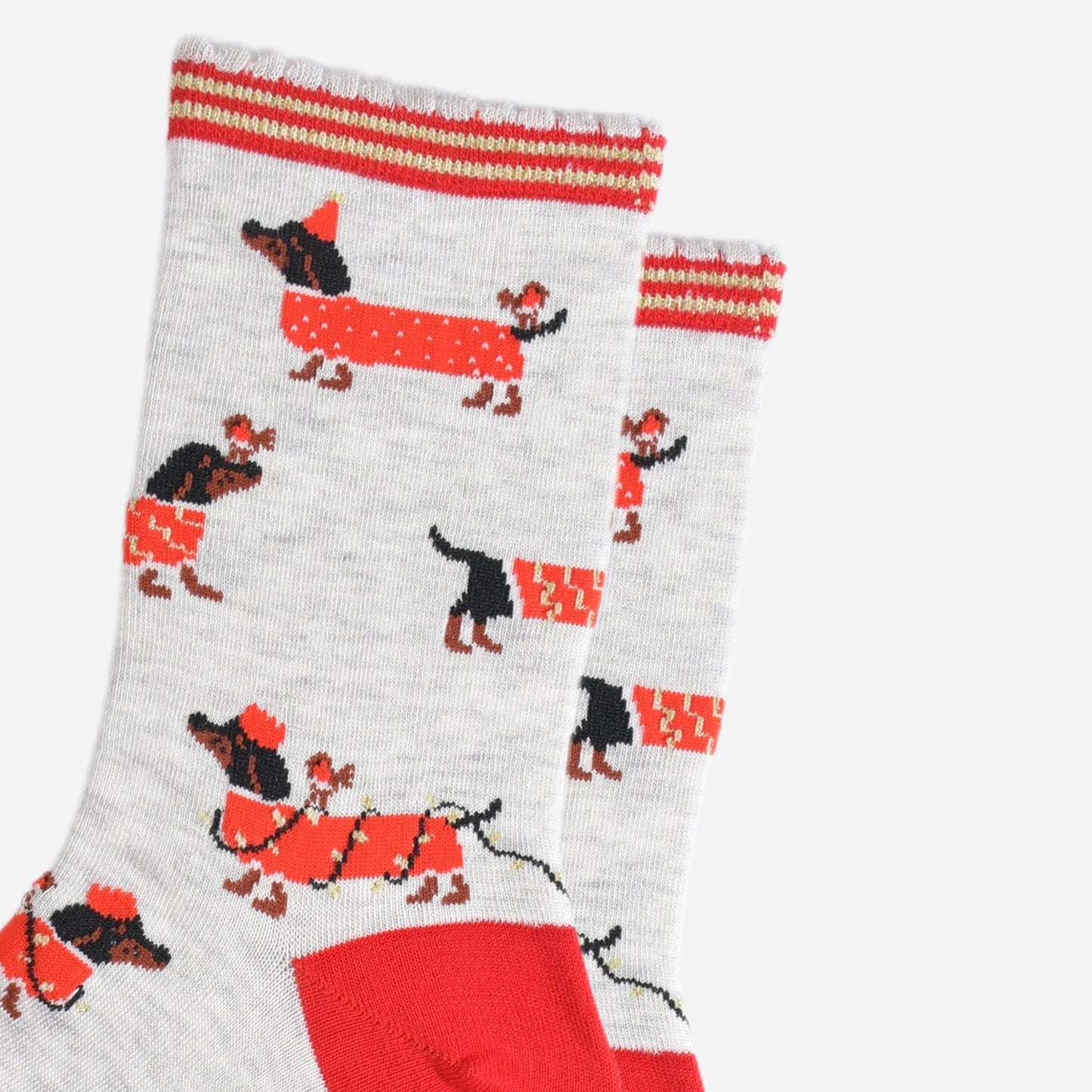 close up of the sausage dog pattern, the dogs are black and wearing red coats. one dog is wearing a red party hat and has a robin on its back. one dog is wrapped in gold party lights and is wearing a red party crown, also with a robin on its back. the last design is a dog wearing a red and gold coat and has a robin sitting on its nose.