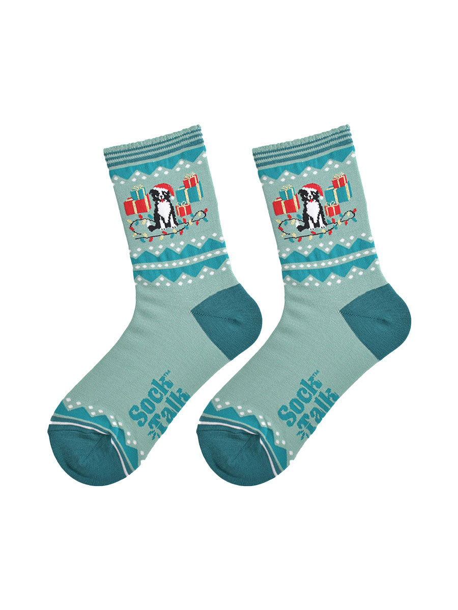 showing the border collie socks laying flat, they are mint and sage green , the dog on the ankles is sitting amongst a pile of red and green xmas gifts and colourful party lights