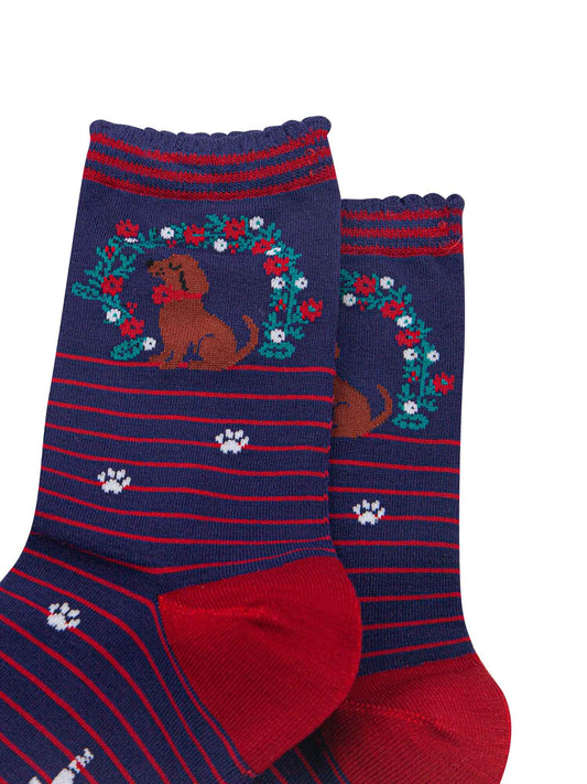 close up of the sausage dog and floral wreath on the ankle of the bamboo socks, the wreath is green with red and white flowers, the dog is brown and is wearing a red collar.