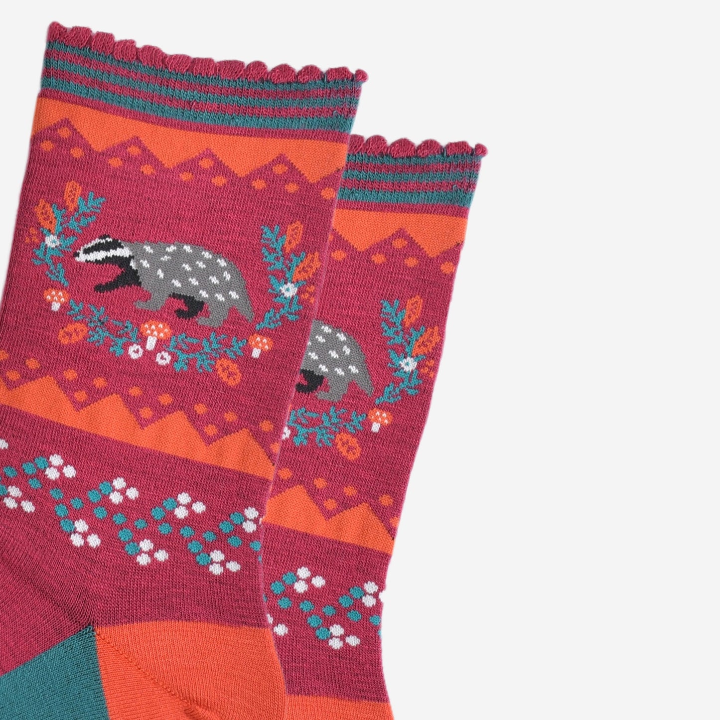 close up of the badger and wreath on the ankle of the socks, the badger is grey and black and the wreath is freen with red toadstool and autumn leaf accents