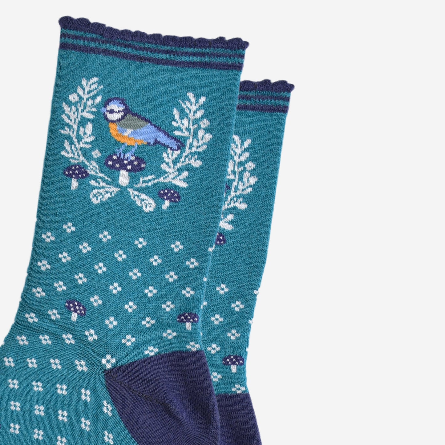 close up of the blue tit bird motif on the ankle of the socks, the bird is perched on a blue toadstool and surrounded by a white horseshoe shaped wreath