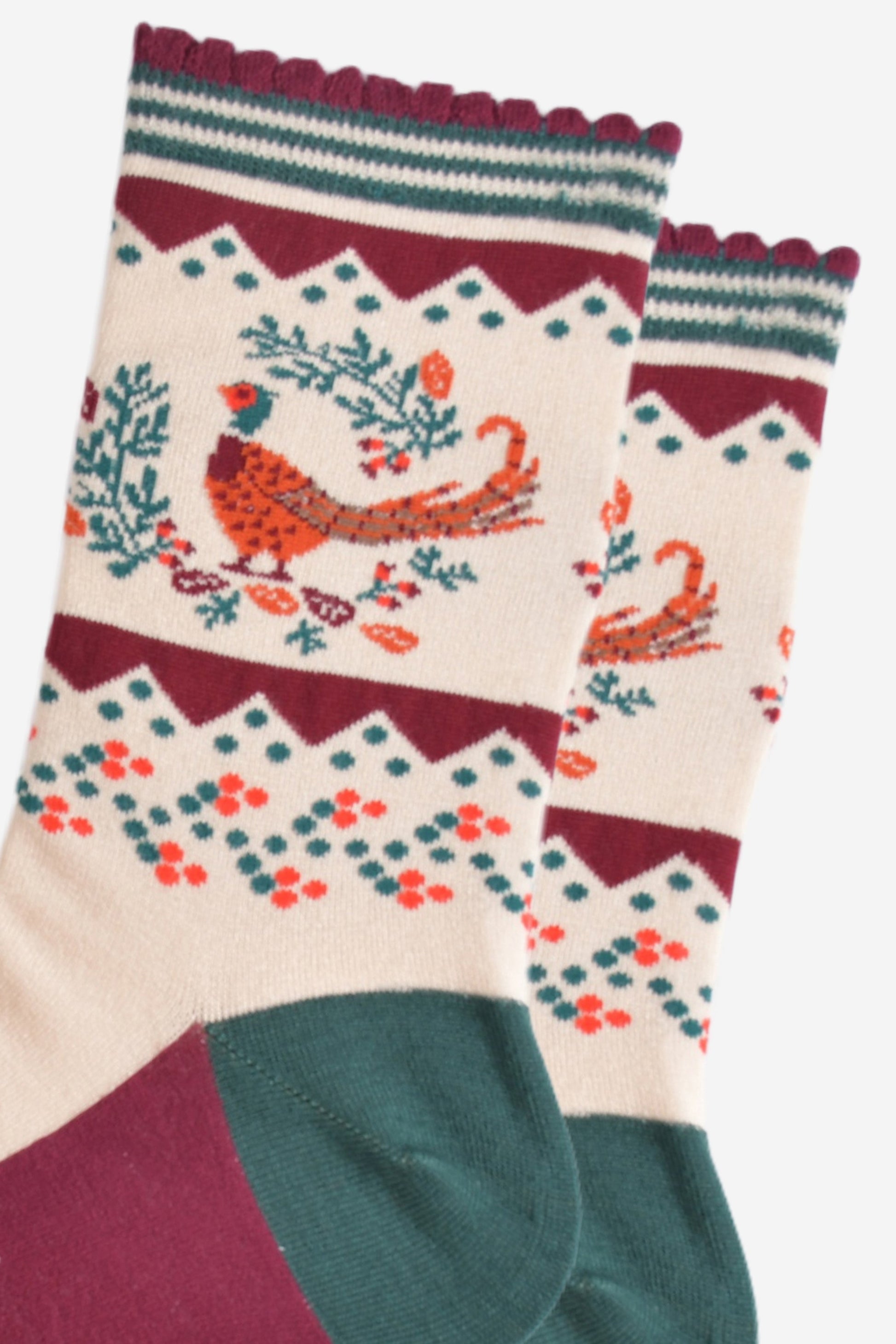 close up of the woodland pheasant and autumnal wreath on the ankle of the socks, the pheasants are stranding in the middle of a green horseshoe shaped wreath, there are orange and red fallen leaves scattered around