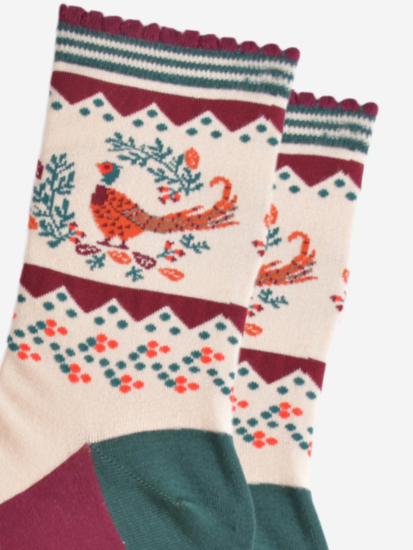 close up of the woodland pheasant and autumnal wreath on the ankle of the socks, the pheasants are stranding in the middle of a green horseshoe shaped wreath, there are orange and red fallen leaves scattered around