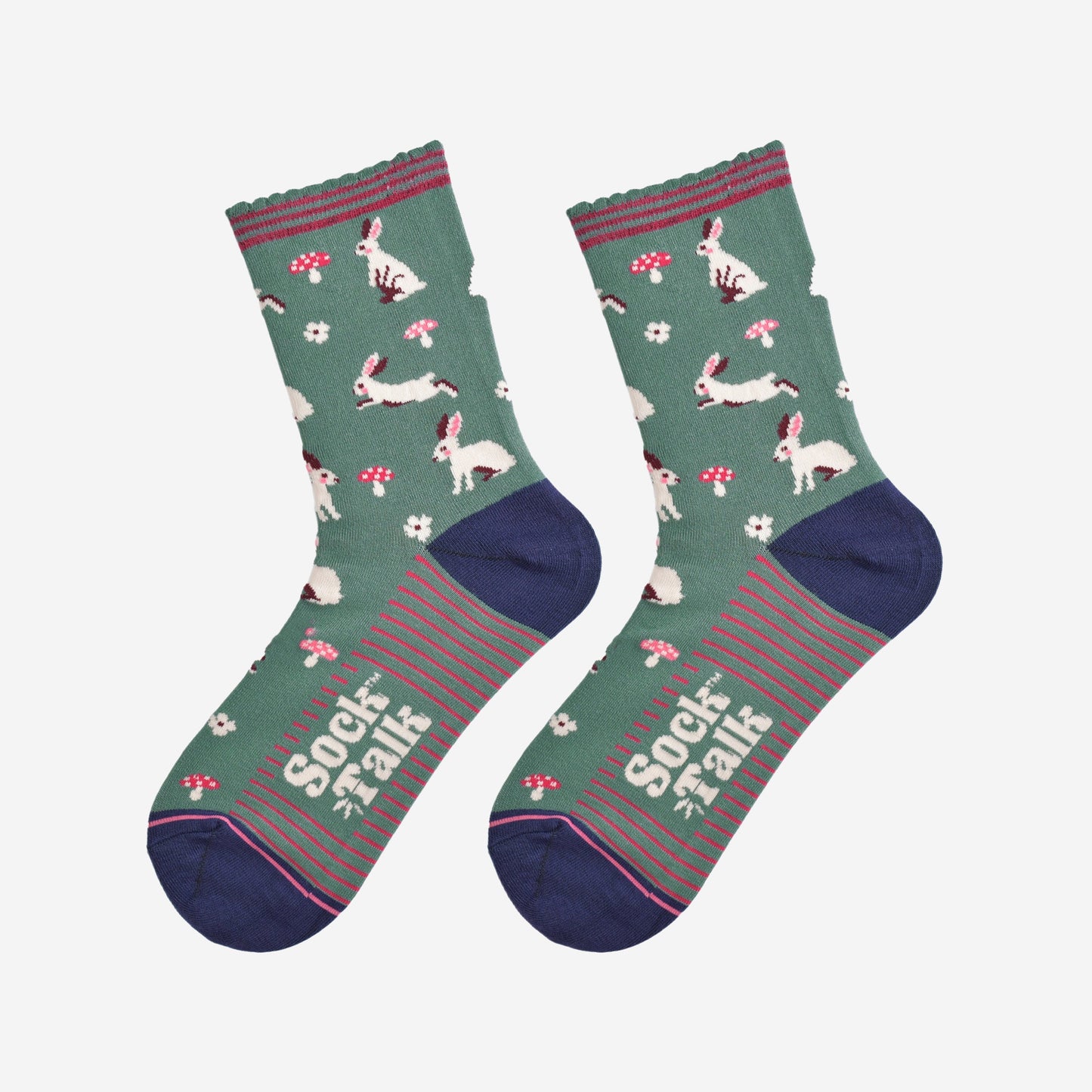 showing the woodland rabbit socks laying flat, there are white rabbits, hopping, sitting and standing among pink toadstools and white flowers, the solve of the socks has pink stripes in contrast to the green base of the design