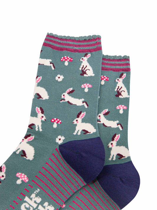 close up of the white rabbit design, the rabbits are sitting, hopping and standing, they have pink rosy cheeks and pink inner ears. there are pink and white toadstools and white flowers scattered around the design.
