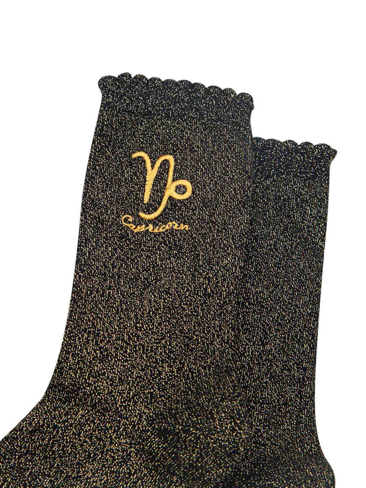 close up of the gold embroidered zodiac detail on the ankle of the socks, showing clearly the symbol of and word capricorn