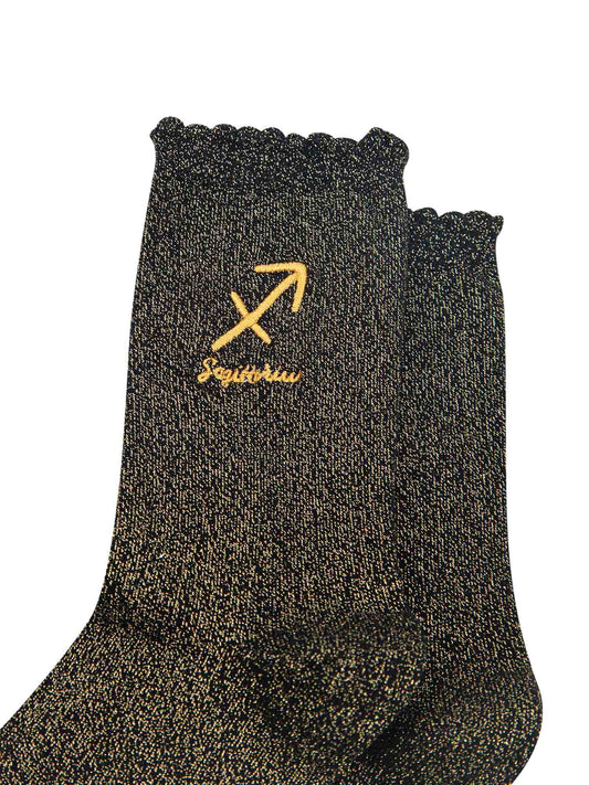 close up of the gold embroidered zodiac detail on the ankle of the socks, showing clearly the symbol of and word sagittarius