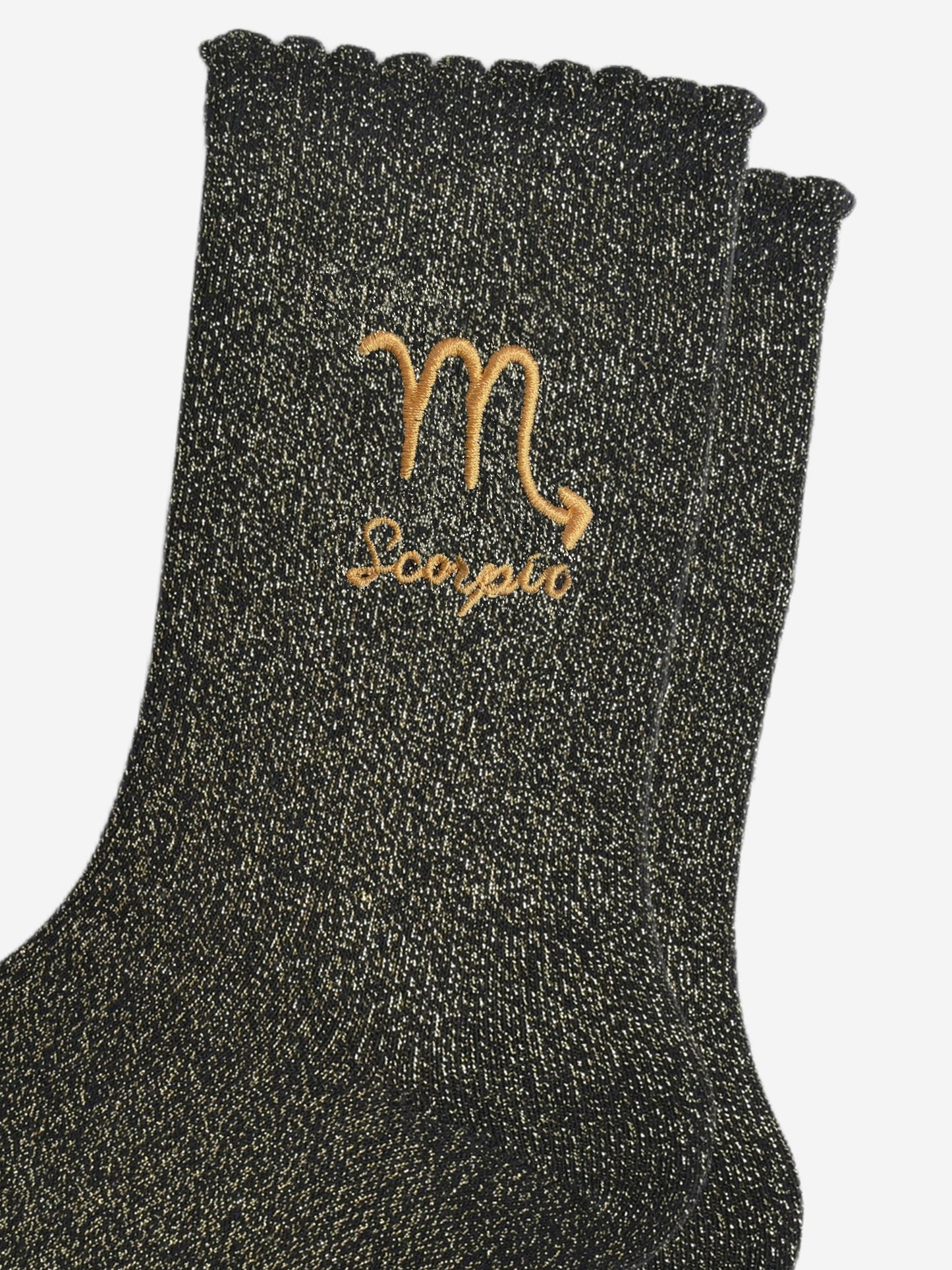 close up of the gold embroidered zodiac detail on the ankle of the socks, showing clearly the symbol of and word scorpio