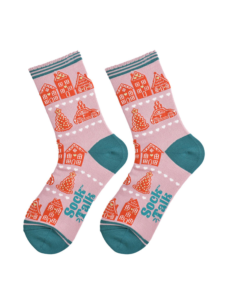 showing the gingerbread house socks laying flat, the pattern is in rows separated by white love heats, the toe and heel of the socks are teal blue in contrast to the light pink background.