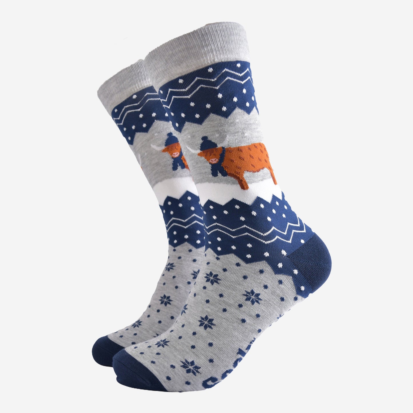 navy blue and grey bamboo socks with a fair isle zig zag and snowflake pattern, featuring a highland cow standing in a snowy field wearing a blue winter hat