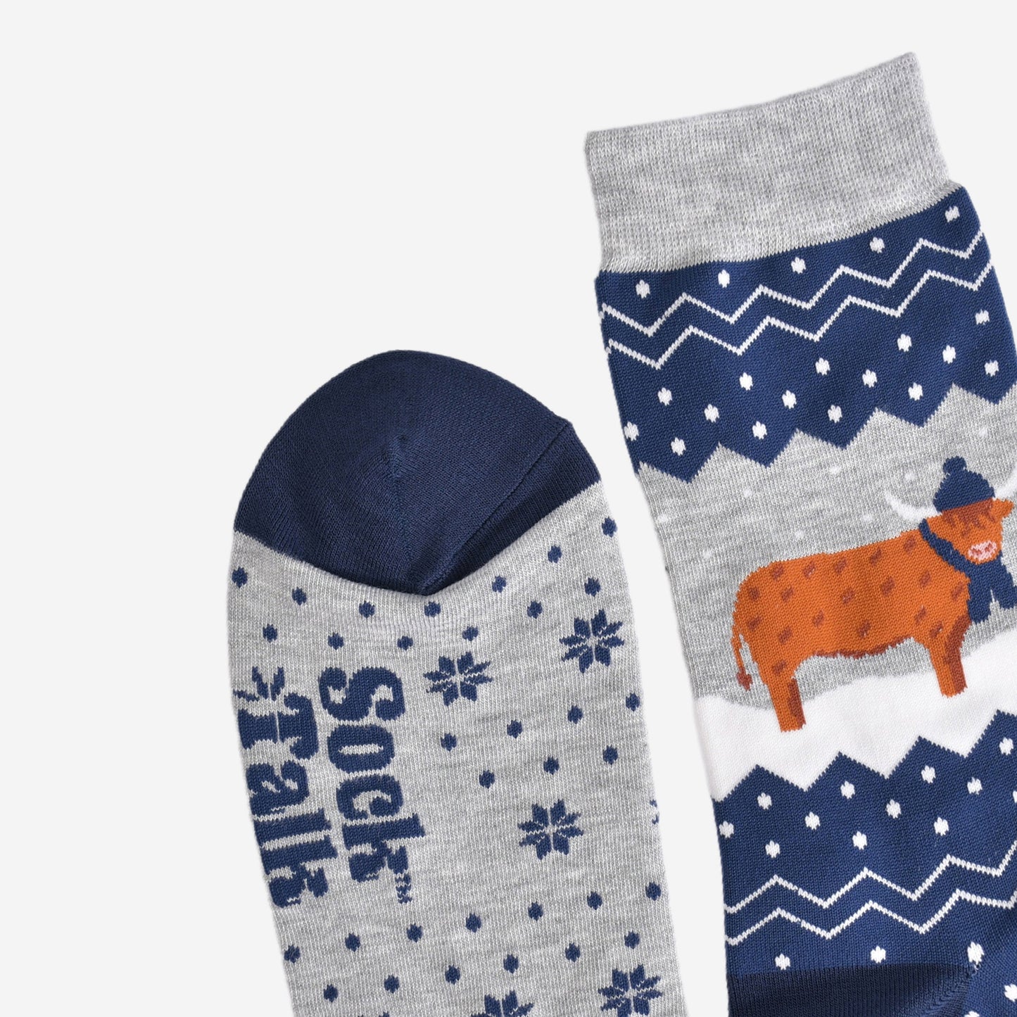 showing the toe and cuff of the socks, showing clearly the fair isle pattern and highland cow, the cow is wearing a winter hat and scarf