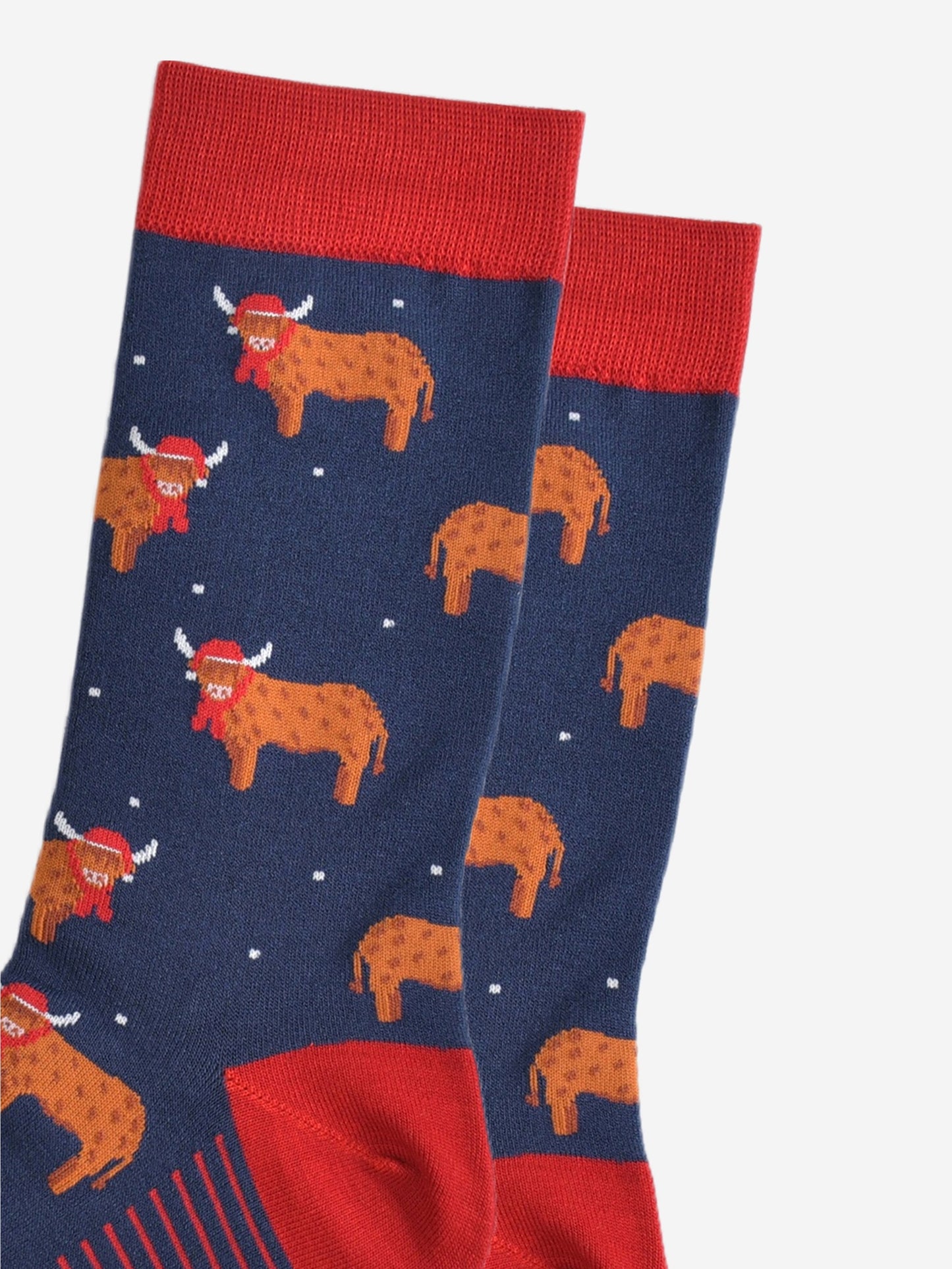 close up of the orange highland cows on the socks, the cows are standing up and they are designed to look like they have long hair, they are also wearing a red santa hat and scarf