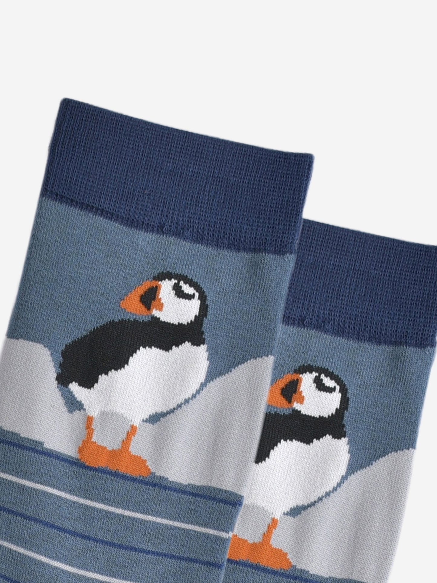 close up of the puffin, it is standing and has white cliffs behind it.