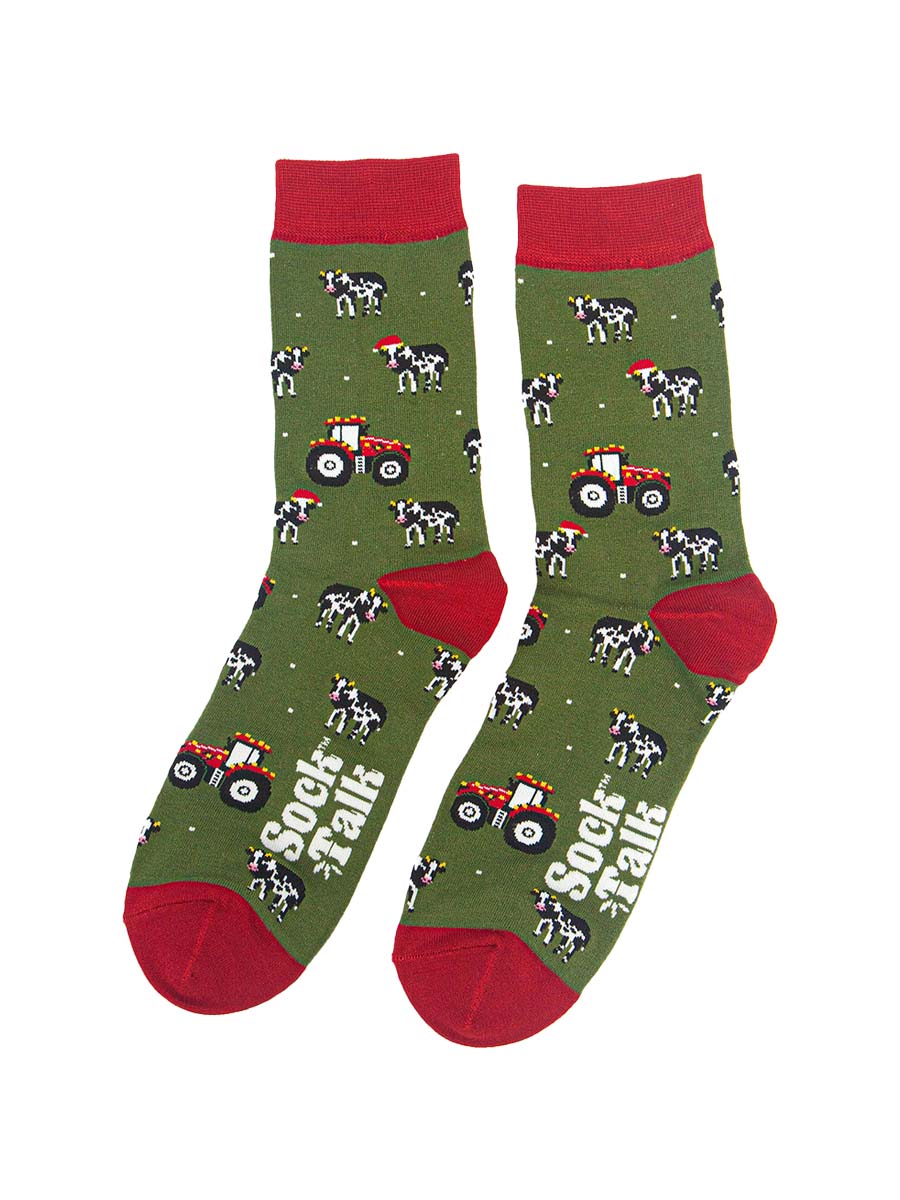 showing the tractor and cow socks laying flat, the cows are black and white with santa hats, the tractors are reed and have party lights on them. the toe, heel and cuff of the socks are red in contrast to the green body of the socks.