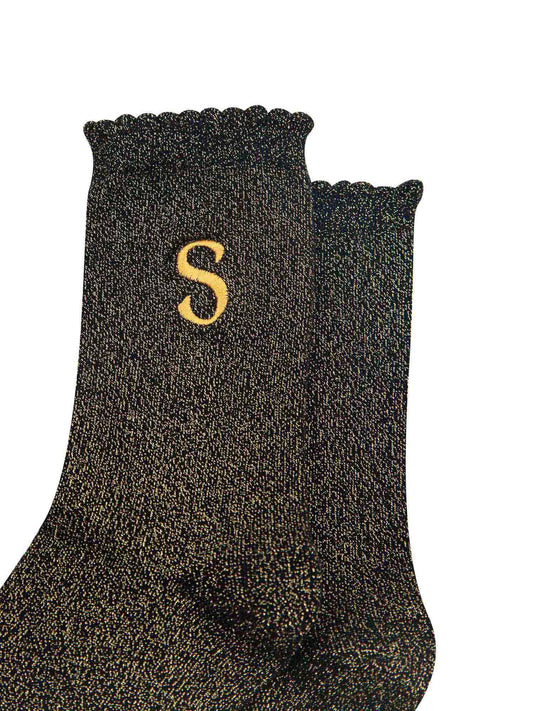 close up of the gold embroidered capital letter s on the ankle of the socks