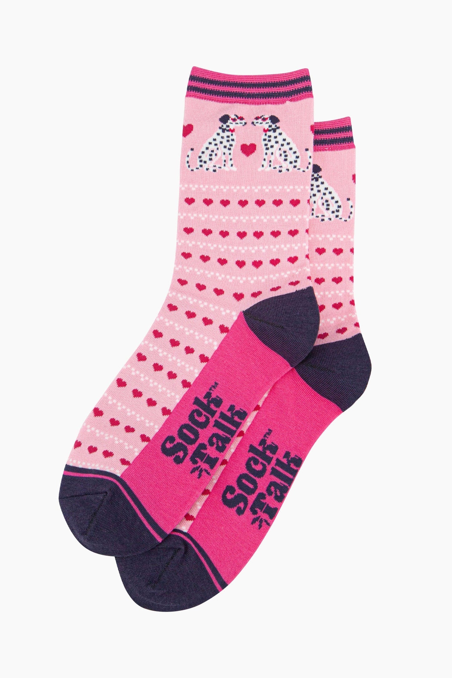 the pair of pink dalmatian dog socks laying flat, one overlapping the other. showing clearly the light pink background of the socks which is contrasted by the repeating rows of fuchsia pink love hearts. the dalmatians feature on the ankle of the socks. the sock talk logo is visible on the base of the sole. 