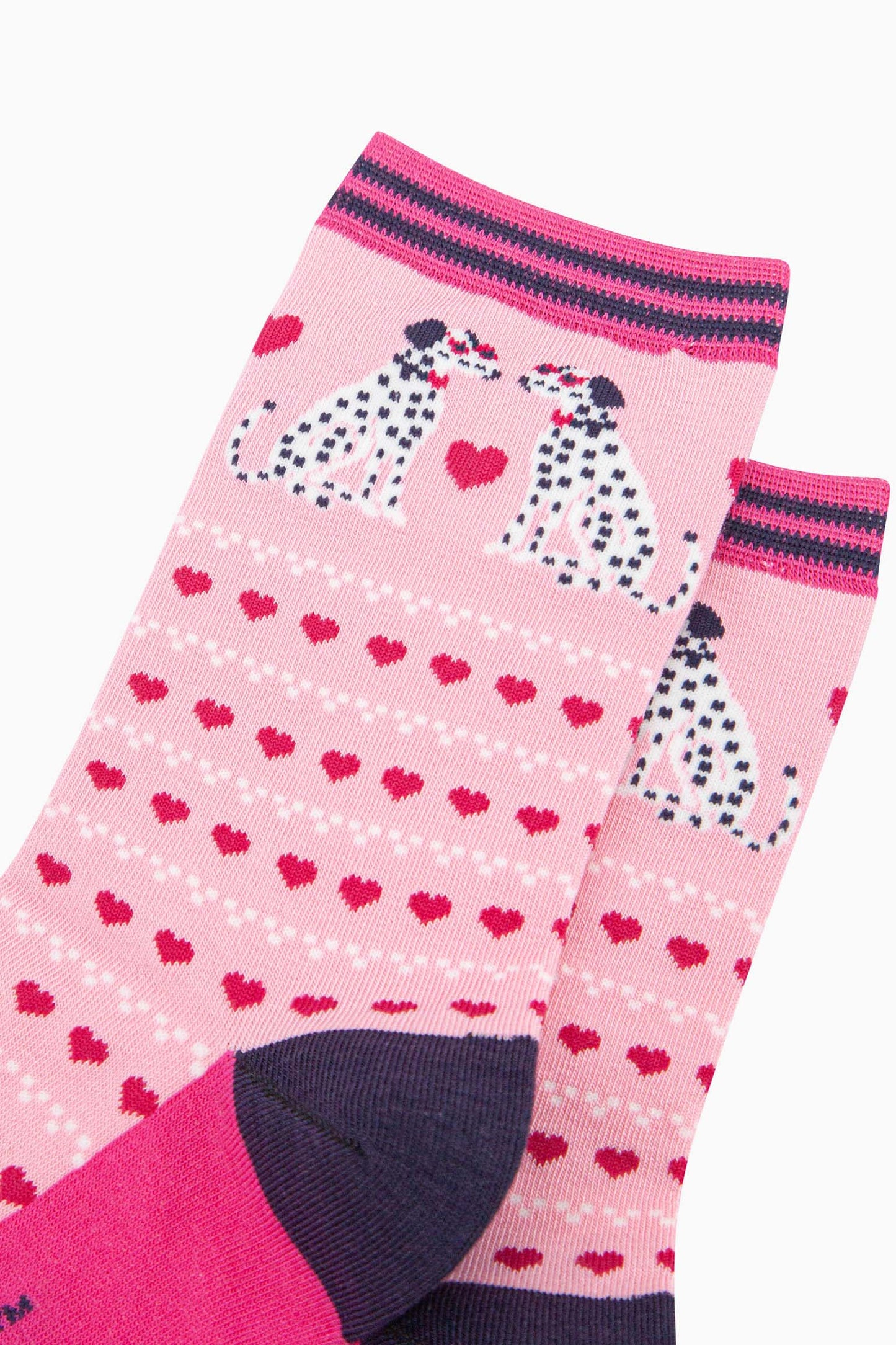 close up of the pattern. the pair of dalmatian dogs on the ankle are facing each other. Each dog is wearing a pair of pink sunglasses and a bowtie. between the sitting dalmatians is a large fuchsia pink love heart. the body of the sock is covered in rows of fuchsia pink love hearts and rows of  white dots.