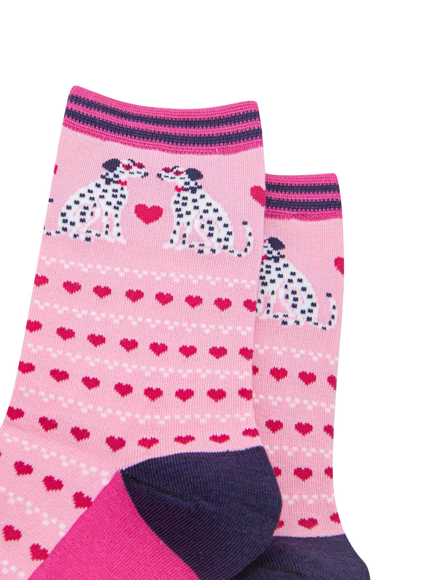 close up of the pattern. the pair of dalmatian dogs on the ankle are facing each other. Each dog is wearing a pair of pink sunglasses and a bowtie. between the sitting dalmatians is a large fuchsia pink love heart. the body of the sock is covered in rows of fuchsia pink love hearts and rows of  white dots.