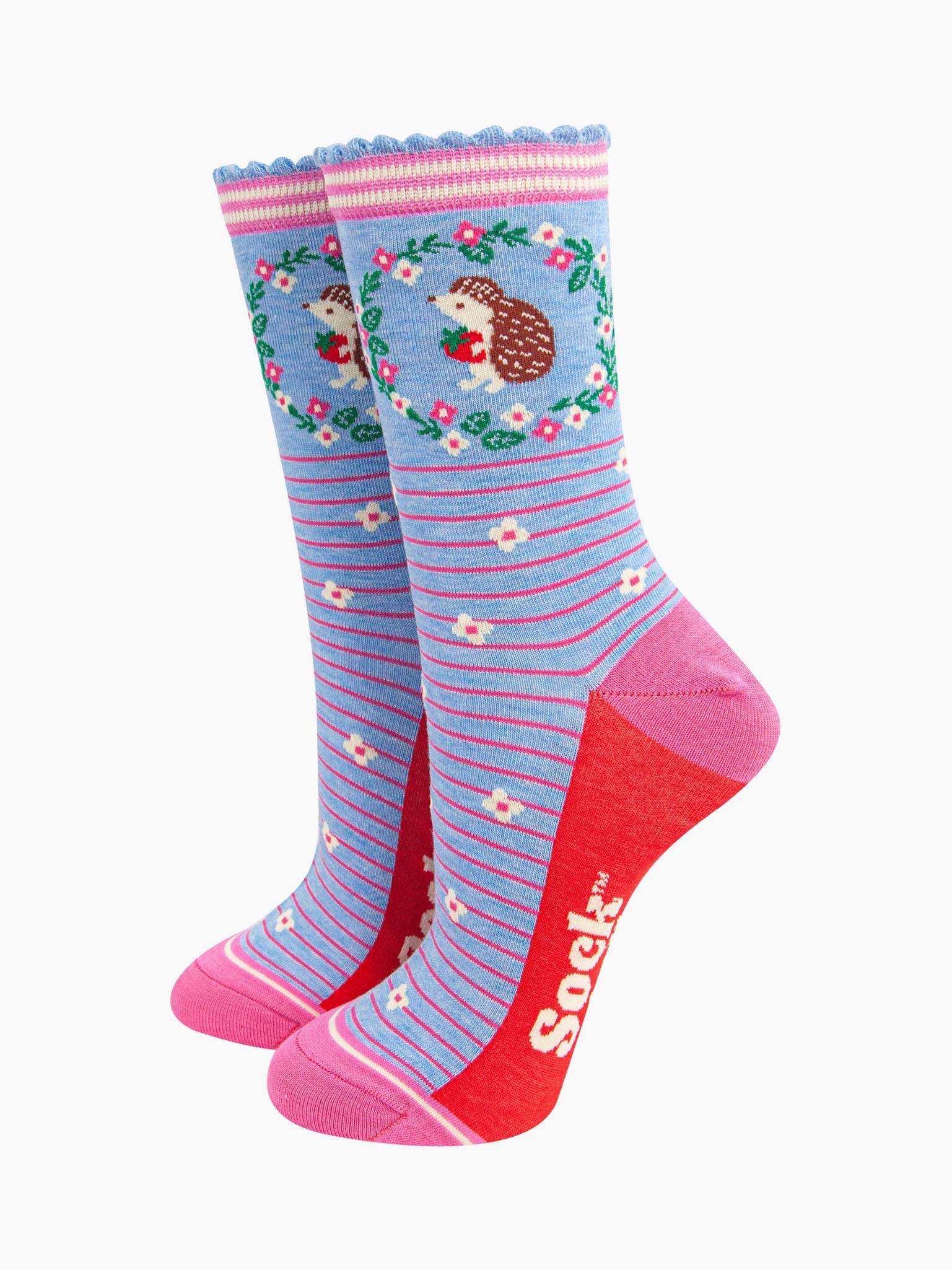 light blue bamboo socks with pink horizontal pinstripes. on the ankle of the socks there is a hedgehog holding a strawberry. around the hedgehog is a pink and white floral wreath.