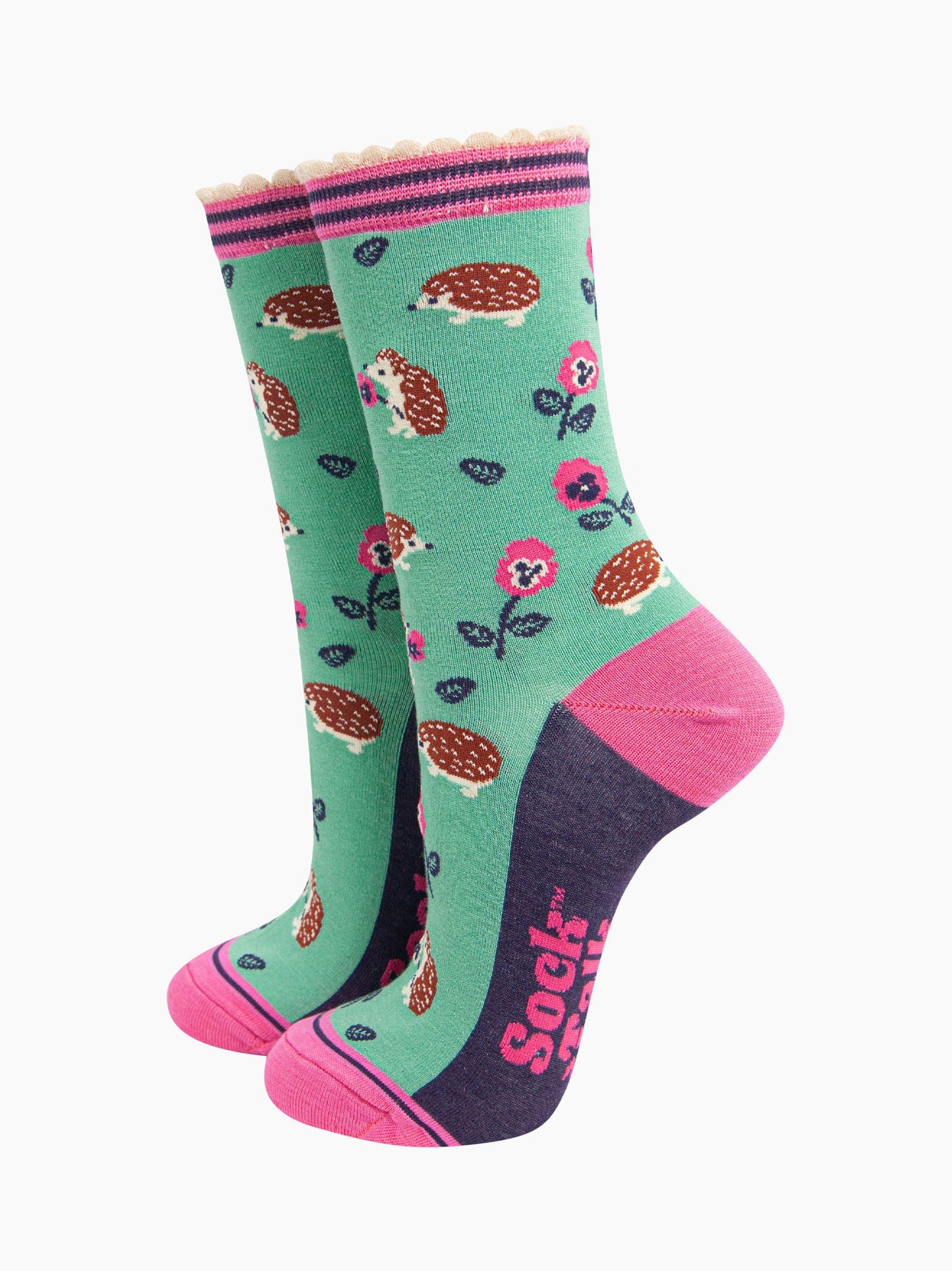 mint green bamboo socks with an all over pattern of woodland hedgehogs and pink pansy flowers. the socks have a contrasting pink heel and toe, the sole is navy blue. the cuff is scalloped and is pink and navy striped.