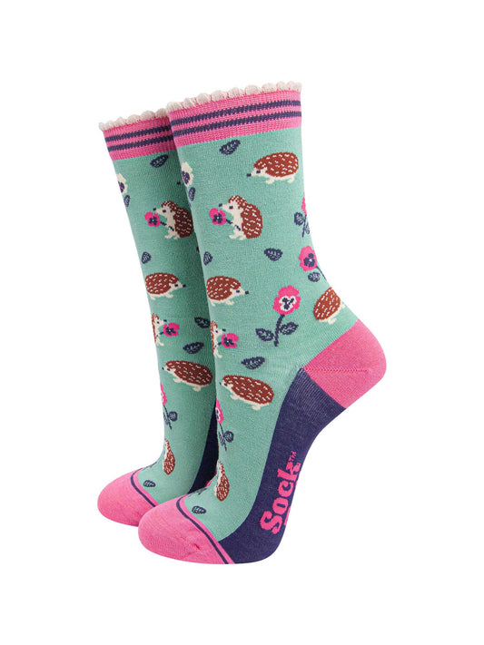 mint green bamboo socks with an all over pattern of woodland hedgehogs and pink pansy flowers. the socks have a contrasting pink heel and toe, the sole is navy blue. the cuff is scalloped and is pink and navy striped.
