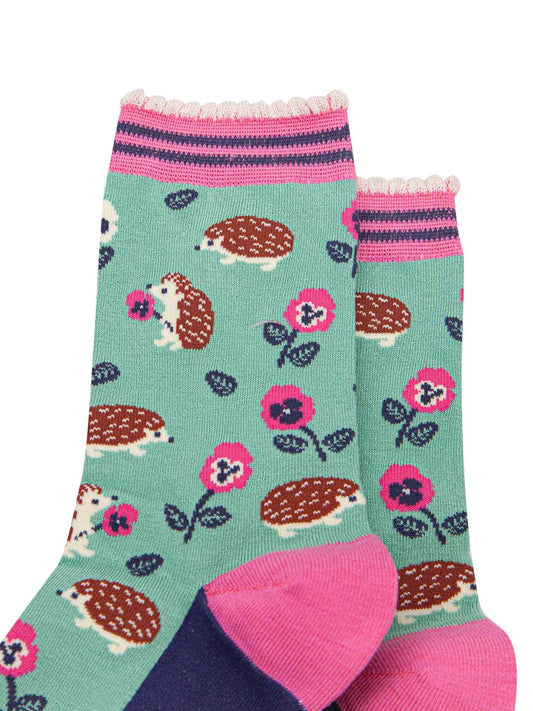 close up of the pattern. the hedgehogs are brown and beige, some are sitting holding pink pansy flowers, others are walking among the flowers. 
