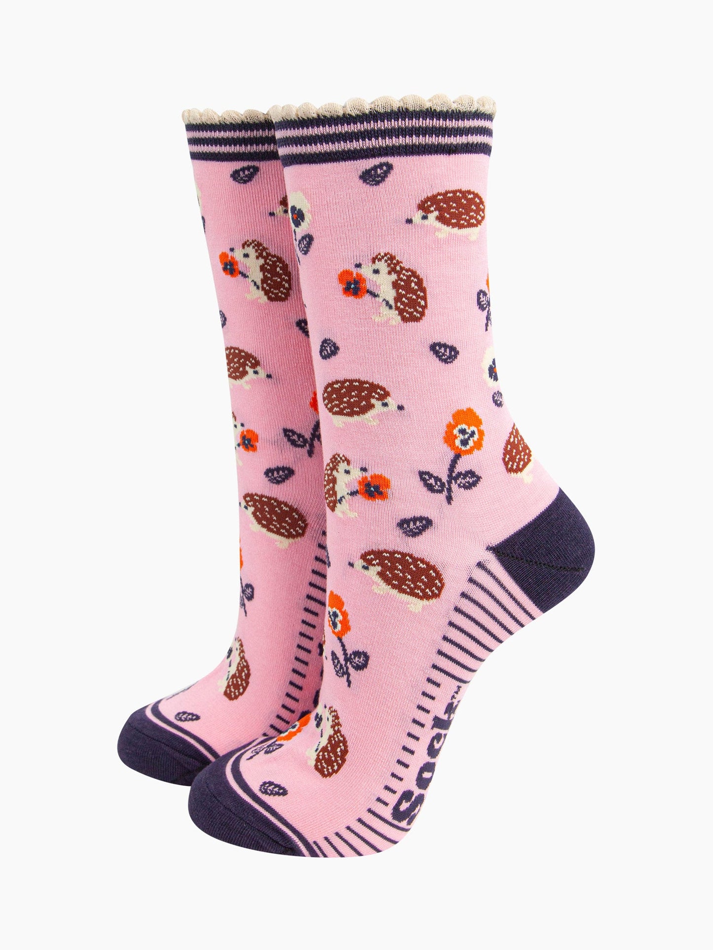  light pink bamboo socks with an all over pattern of woodland hedgehogs and orange pansy flowers. the socks have a contrasting navy blue heel and toe. the cuff is scalloped and is pink and navy striped.