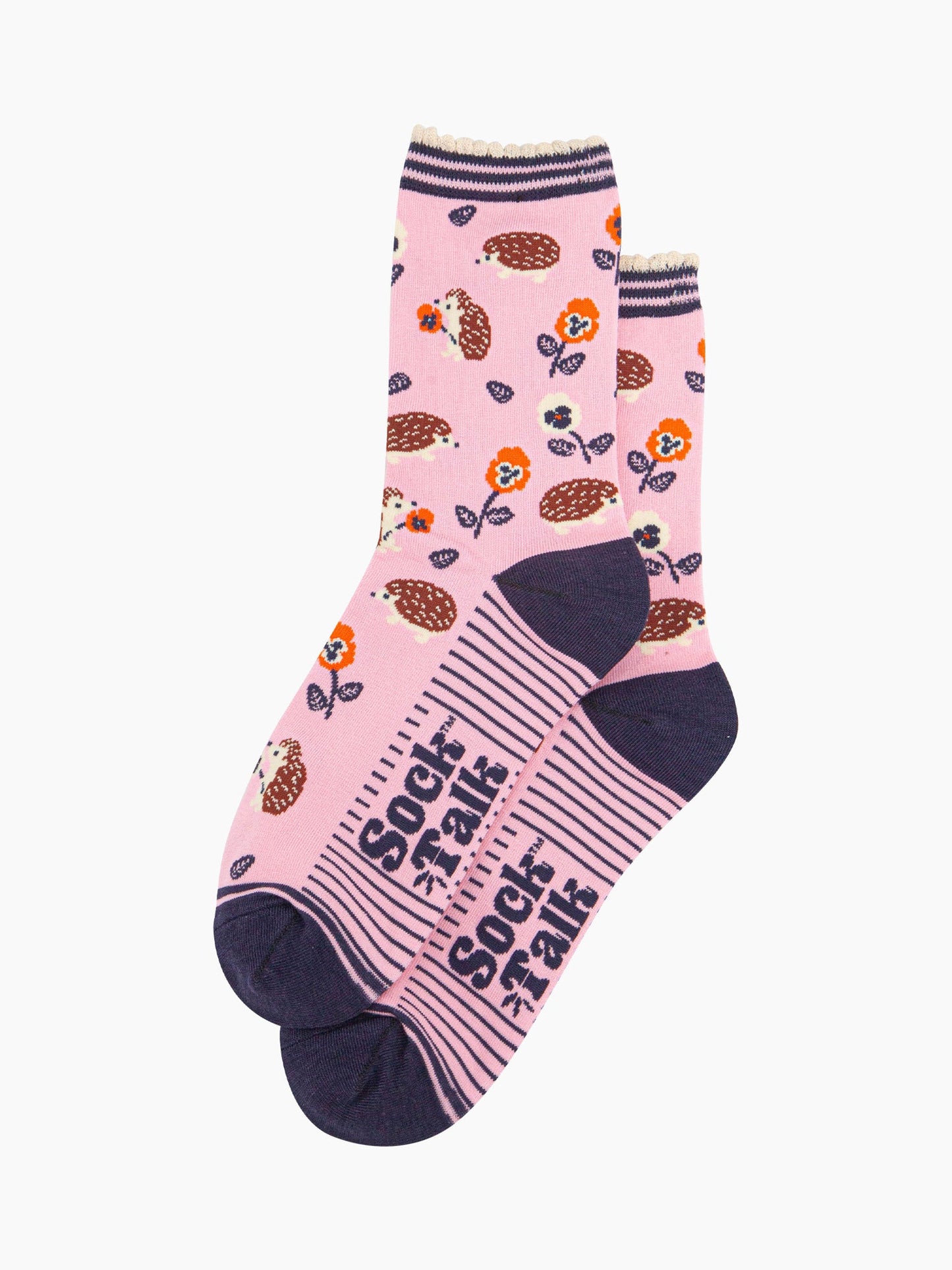 the pair of light pink hedgehog socks laying flat one overlapping the other. showing clearly the pink background of the socks which is contrasted by the all over pattern of hedgehogs, flowers and leaves.  the sock talk logo is navy blue and visible on the base of the sole. 