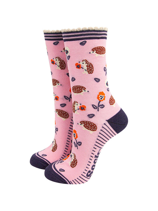 light pink bamboo socks with an all over pattern of woodland hedgehogs and orange pansy flowers. the socks have a contrasting navy blue heel and toe. the cuff is scalloped and is pink and navy striped.
