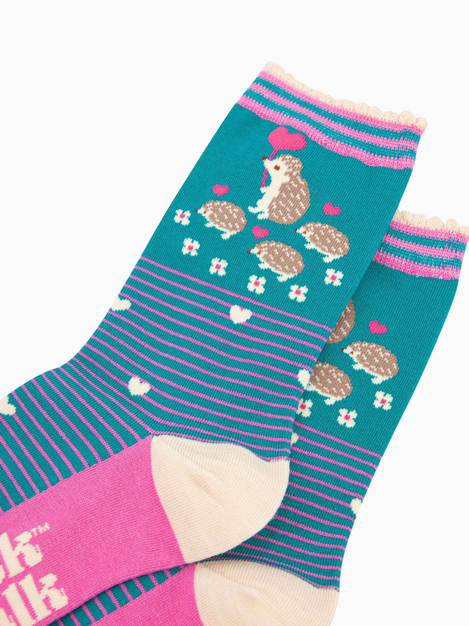 close up of the pattern. there are four hedgehogs on the ankle, one adult and three babies they are beige and each are carrying a fuchsia pink love heart shaped balloon. there are six small white flowers in a semi circle around the bottom of the family. the body of the socks has pink pinstripes and scattered white love hearts.