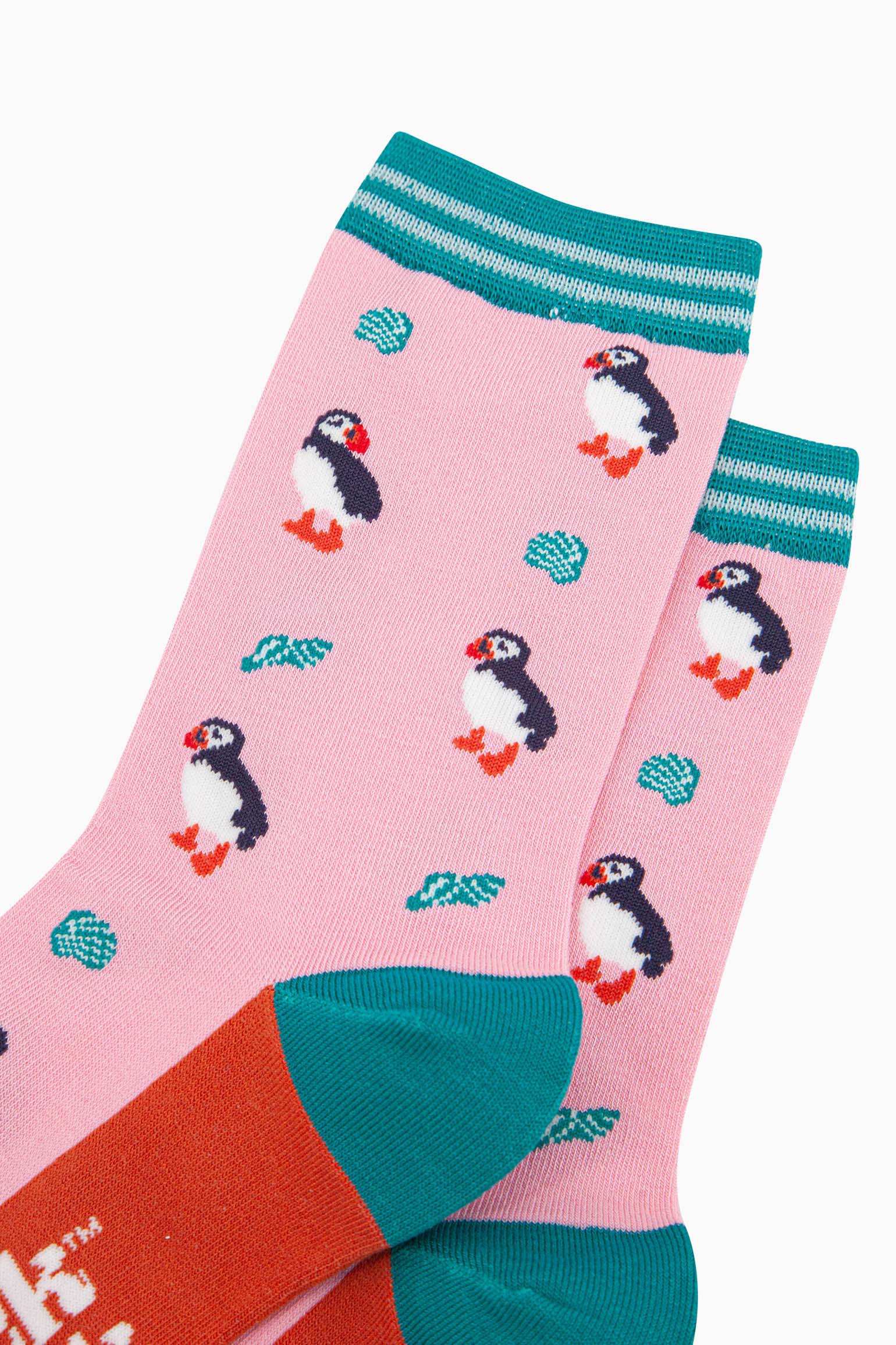 close up of the pattern. the puffin birds are black with white bellies and have orange and red beaks. the seashells are turquoise with white accents. the pattern contrasts the light pink background.