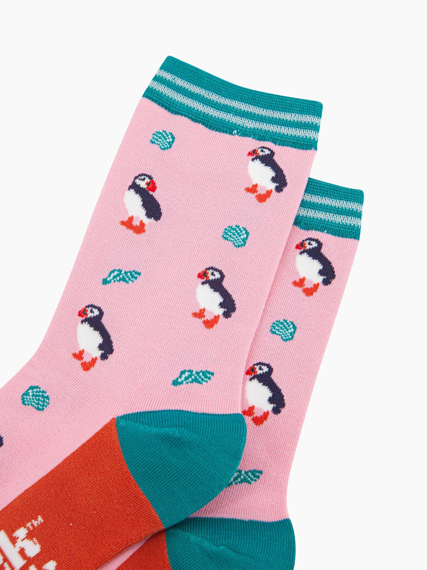 close up of the pattern. the puffin birds are black with white bellies and have orange and red beaks. the seashells are turquoise with white accents. the pattern contrasts the light pink background.