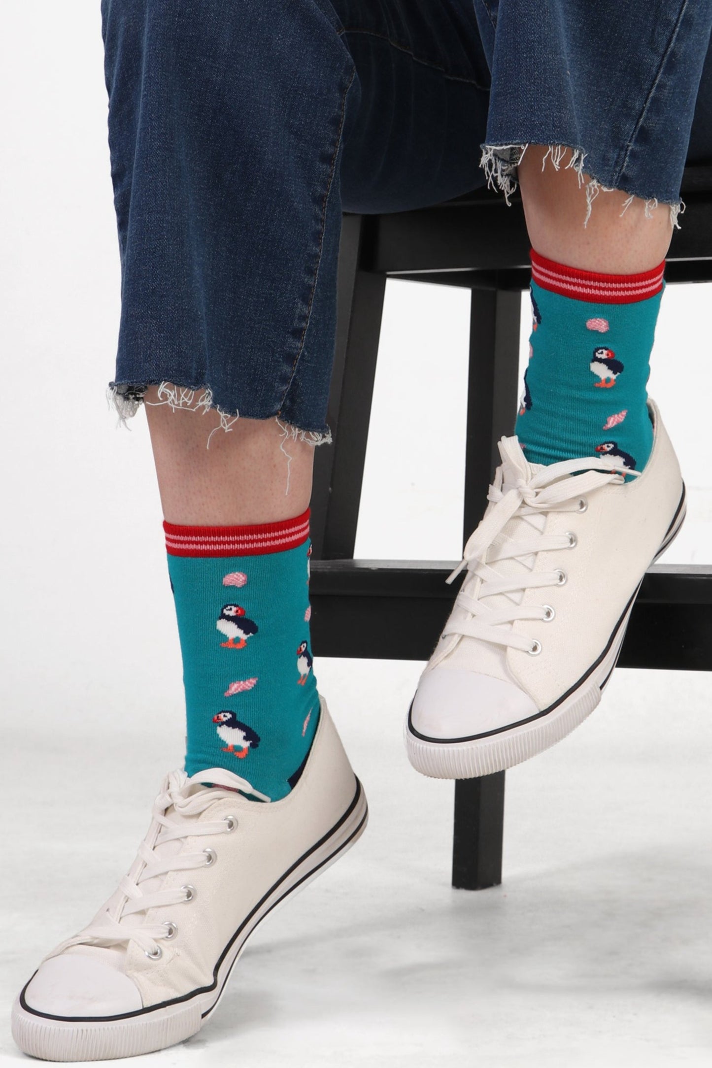 Women's model feet wearing blue puffin print bamboo socks with white trainers