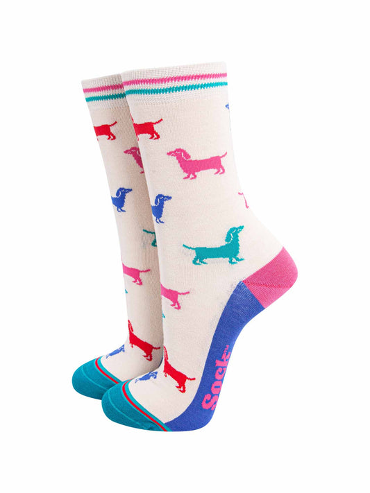 cream bamboo socks with a pattern of colourful sausage dogs. the sole is blue, heel is pink and the toe is turquoise. the cuff of the socks is straight cut and has a turquoise and pink stripe.