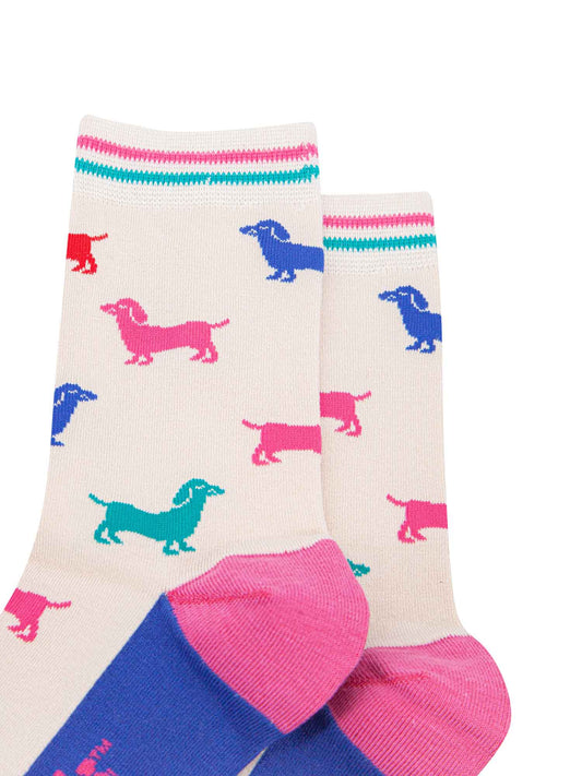 close up of the pattern. the sausage dogs are a variety of bold colours, royal blue, turquoise, pink and red. the cuff has a pink and a turquoise horizontal stripe which contrasts the cream background of the socks.