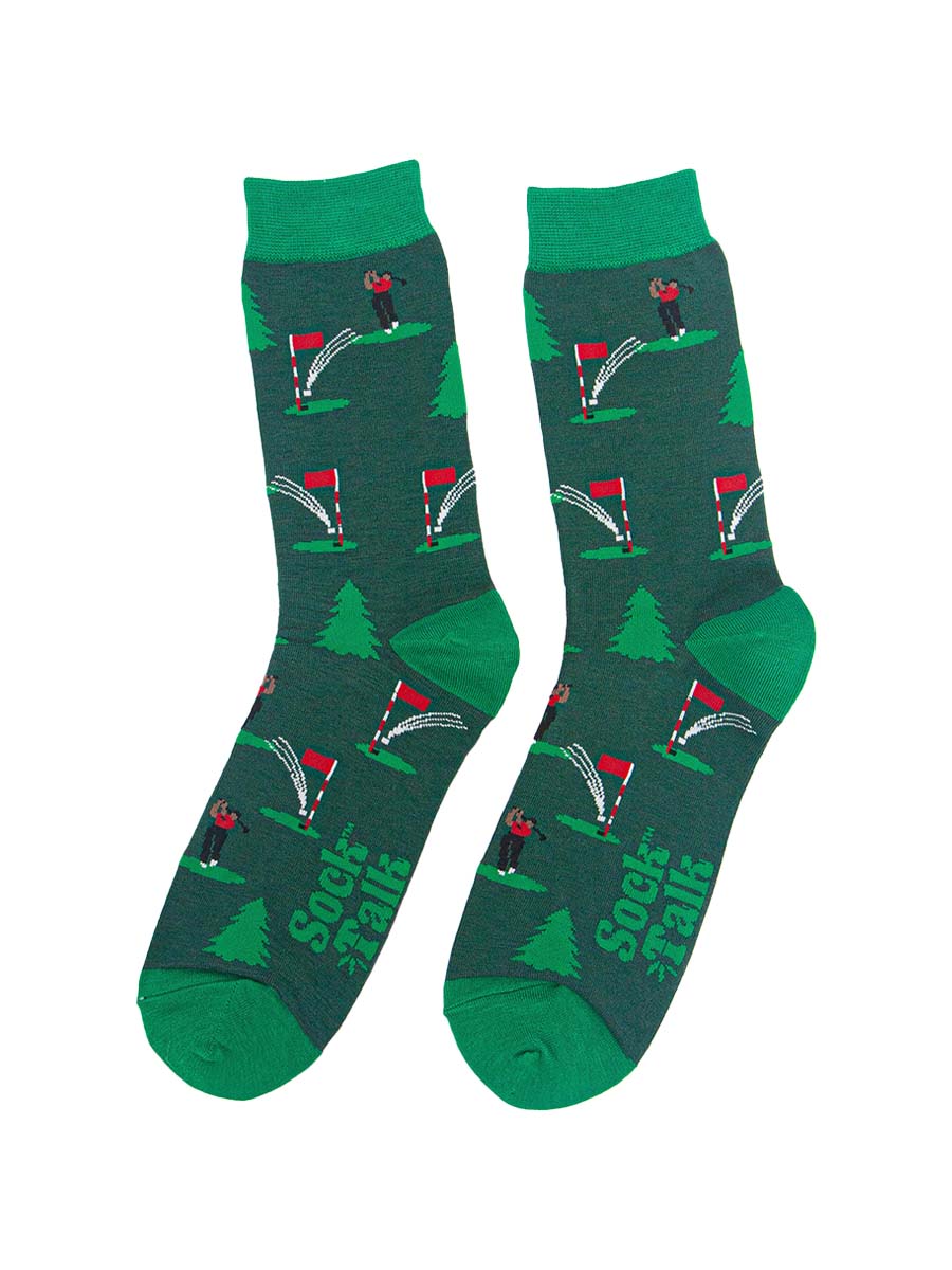 showing the socks laying flat, the golfer chipping the ball into the hole is visible all over the socks, there are also evergreen trees in the pattern