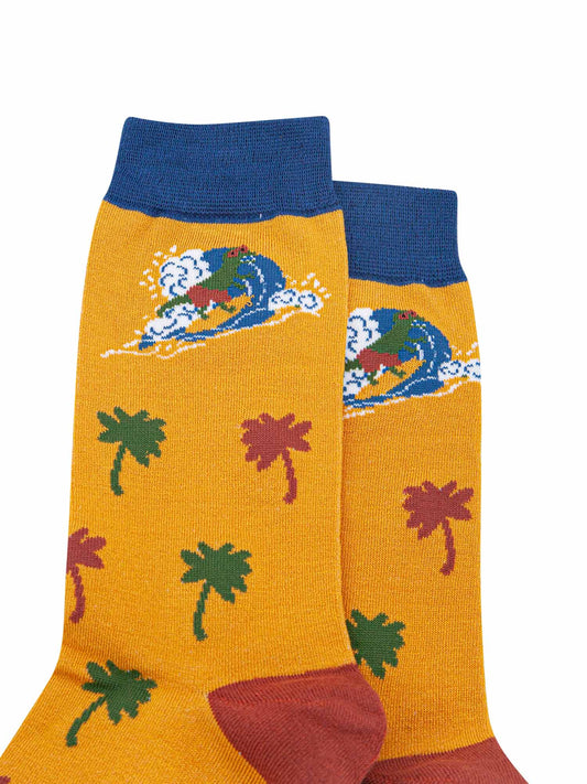 close up of the surfing dinosaur and palm tree design on the yellow and navy blue bamboo socks