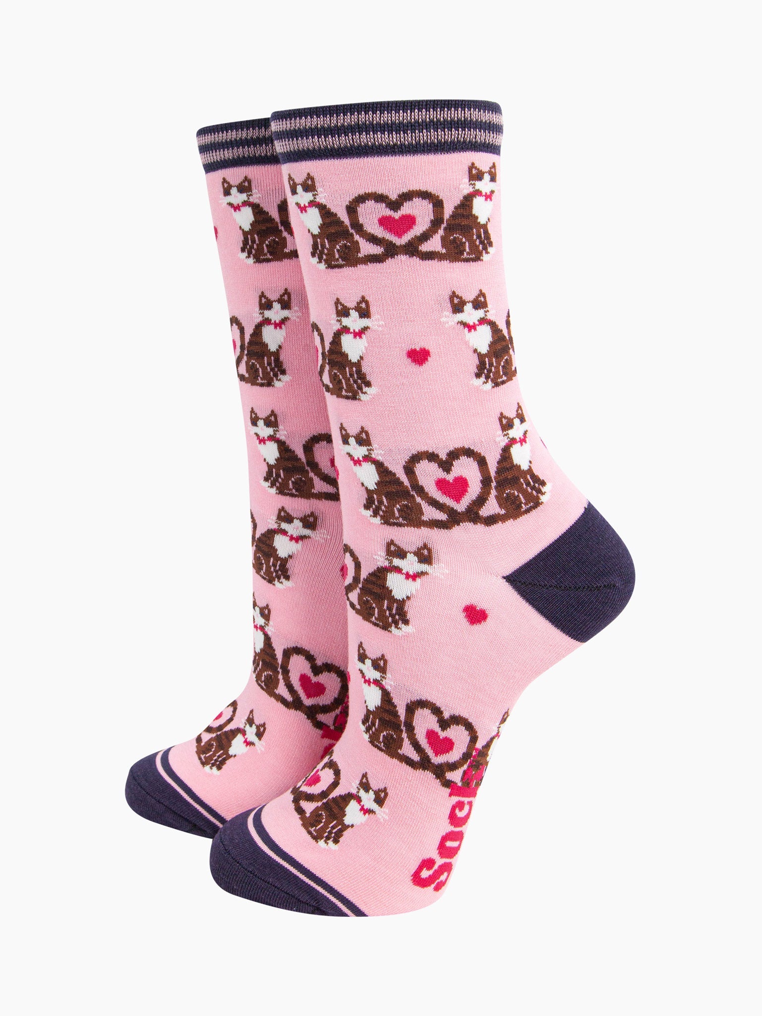 the pair of pink cat and love heart socks laying flat, one overlapping the other. showing clearly the light pink background of the socks which is contrasted by the all over pattern of cats and hearts. the sock talk logo is visible on the base of the sole. 