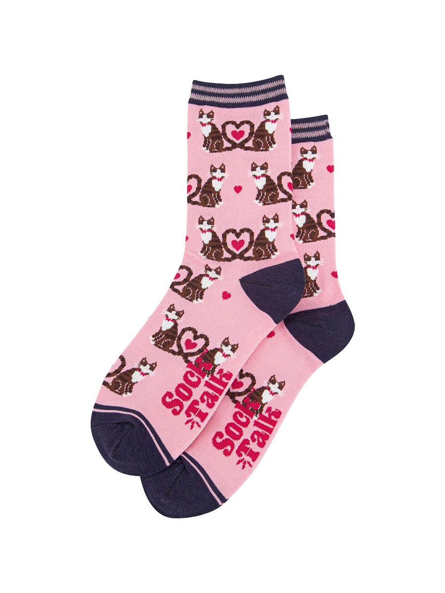the pair of pink cat and love heart socks laying flat, one overlapping the other. showing clearly the light pink background of the socks which is contrasted by the all over pattern of cats and hearts. the sock talk logo is visible on the base of the sole. 